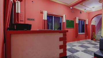 Un espace d’accueil avec un comptoir rouge, un escalier et un sol à carreaux.