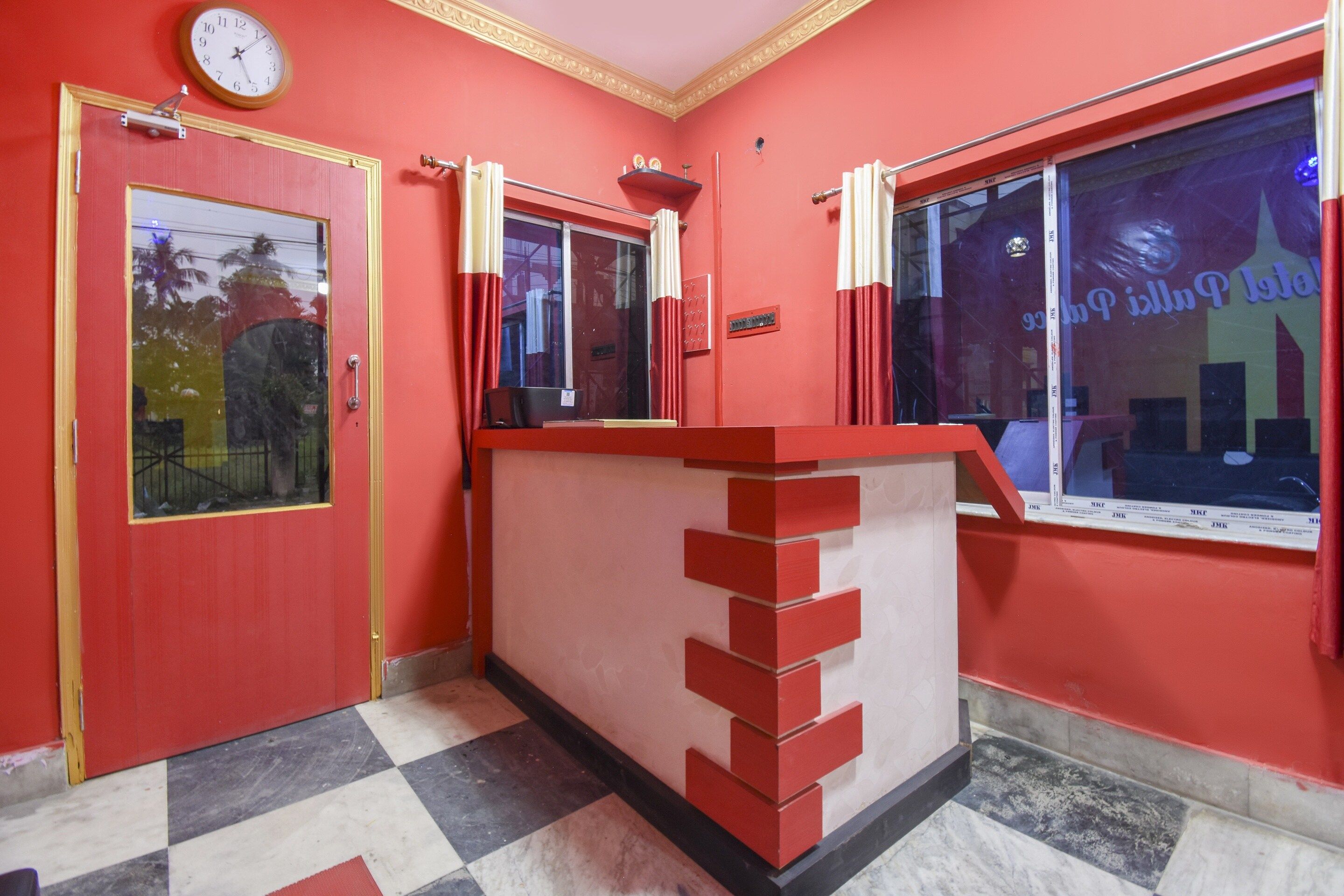 Un espace d’accueil avec un comptoir rouge, une horloge et une fenêtre qui reflète l’environnement.