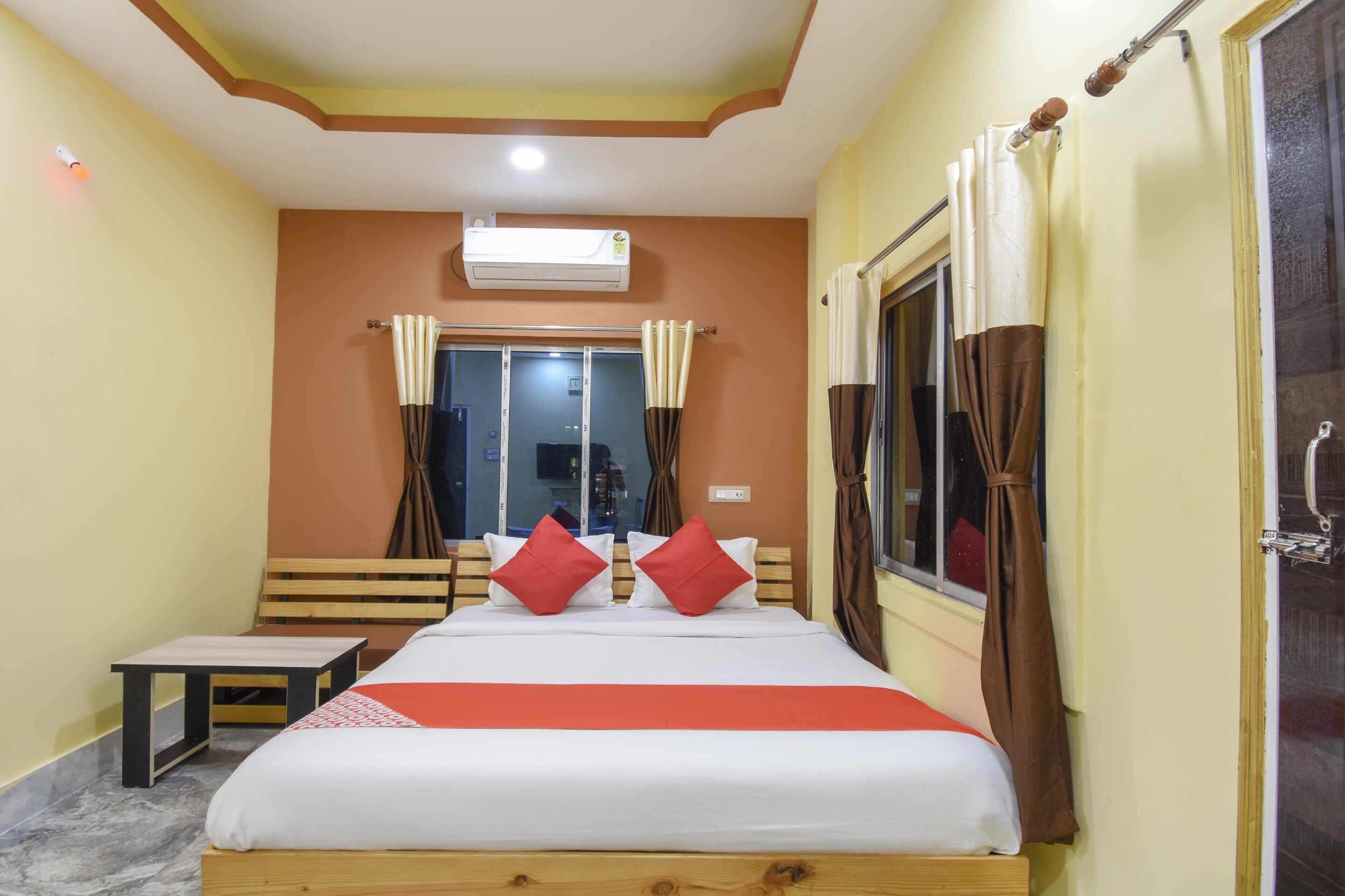Une chambre d’hôtel avec un lit, une petite table, une fenêtre avec des rideaux et un appareil de climatisation fixé au mur.