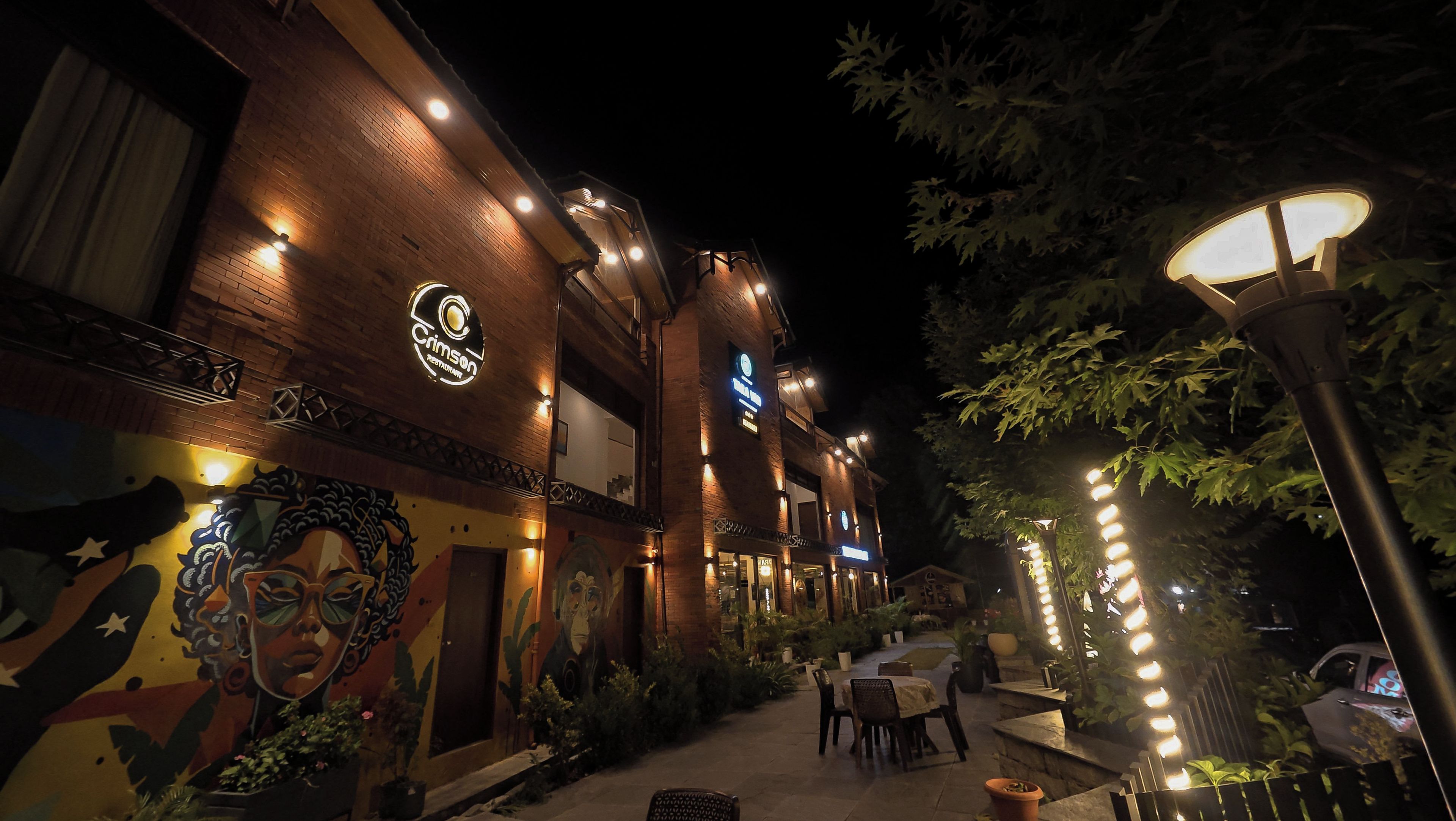 A restaurant with outdoor seating, a mural on the wall, and a sign for 'Cimson Restaurant'.