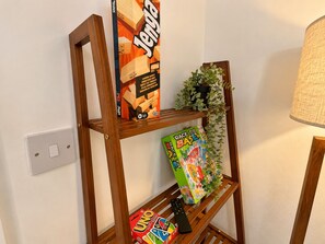 Ein Holzregal mit einem Gesellschaftsspiel, einer Fernbedienung und einer Pflanze.