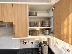 A kitchen with wooden cabinets, a built-in espresso machine, and various bowls and plates on shelves. - 4BR 2BA House | FREE Parking | Near Elizabeth Line (London)