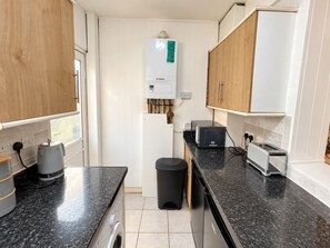 Eine kompakte Küche mit Waschmaschine, Mülleimer, Toaster und Durchlauferhitzer.