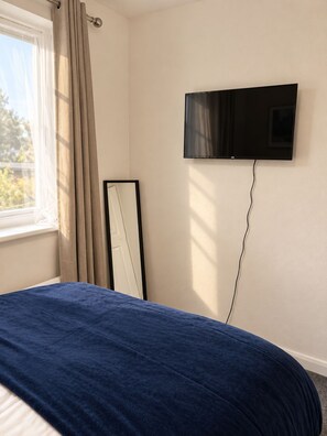 Quarto com cama, televisão na parede e janela com cortinas.