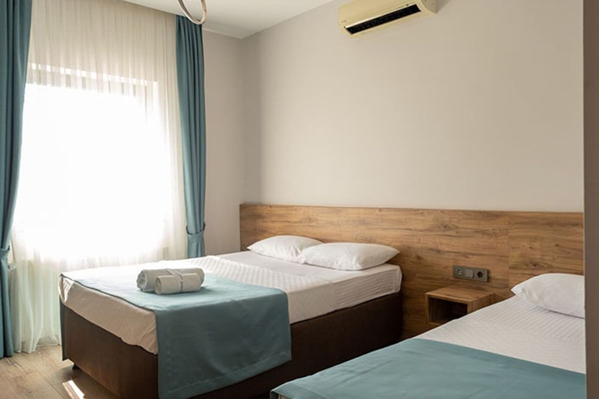 Una camera d'albergo con due letti, una testiera in legno, una finestra con tende e un condizionatore d'aria.