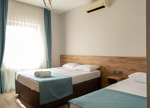 Una camera d'albergo con due letti, una testiera in legno, una finestra con tende e un condizionatore d'aria.
