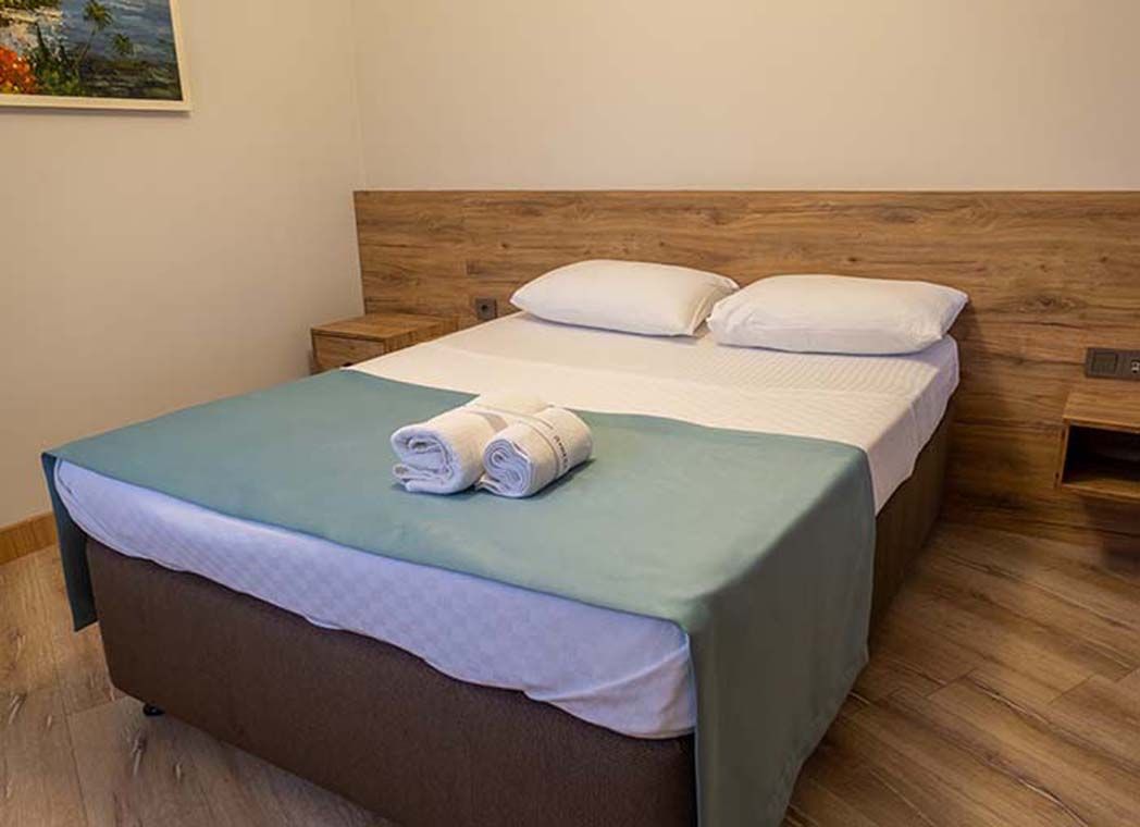 A single bed with a wooden headboard, a green bedspread, and two white pillows.