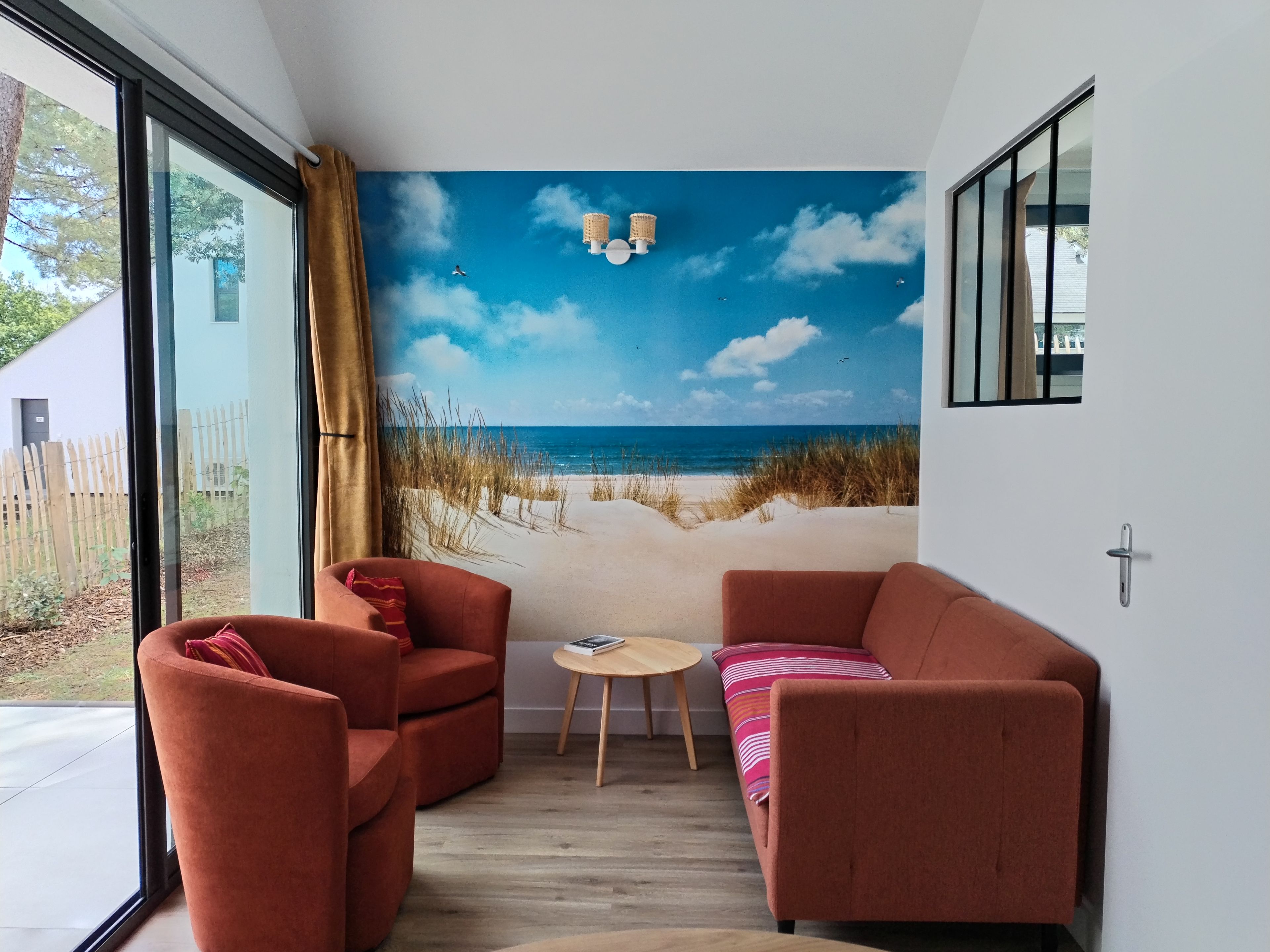 Habitación con un mural de playa, dos sofás rojos, una mesa redonda pequeña y una ventana con cortinas.
