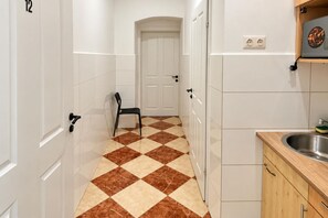 A hallway with a checkered floor, a door, a chair, and a kitchen area with cabinets and a sink. - Drop Your Bags Discover Vienna near Westbahnhof (Vienna)