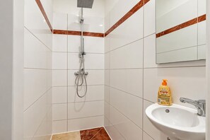 A bathroom with white tiles, a shower, a sink, and a bottle of soap. - Drop Your Bags Discover Vienna near Westbahnhof (Vienna)