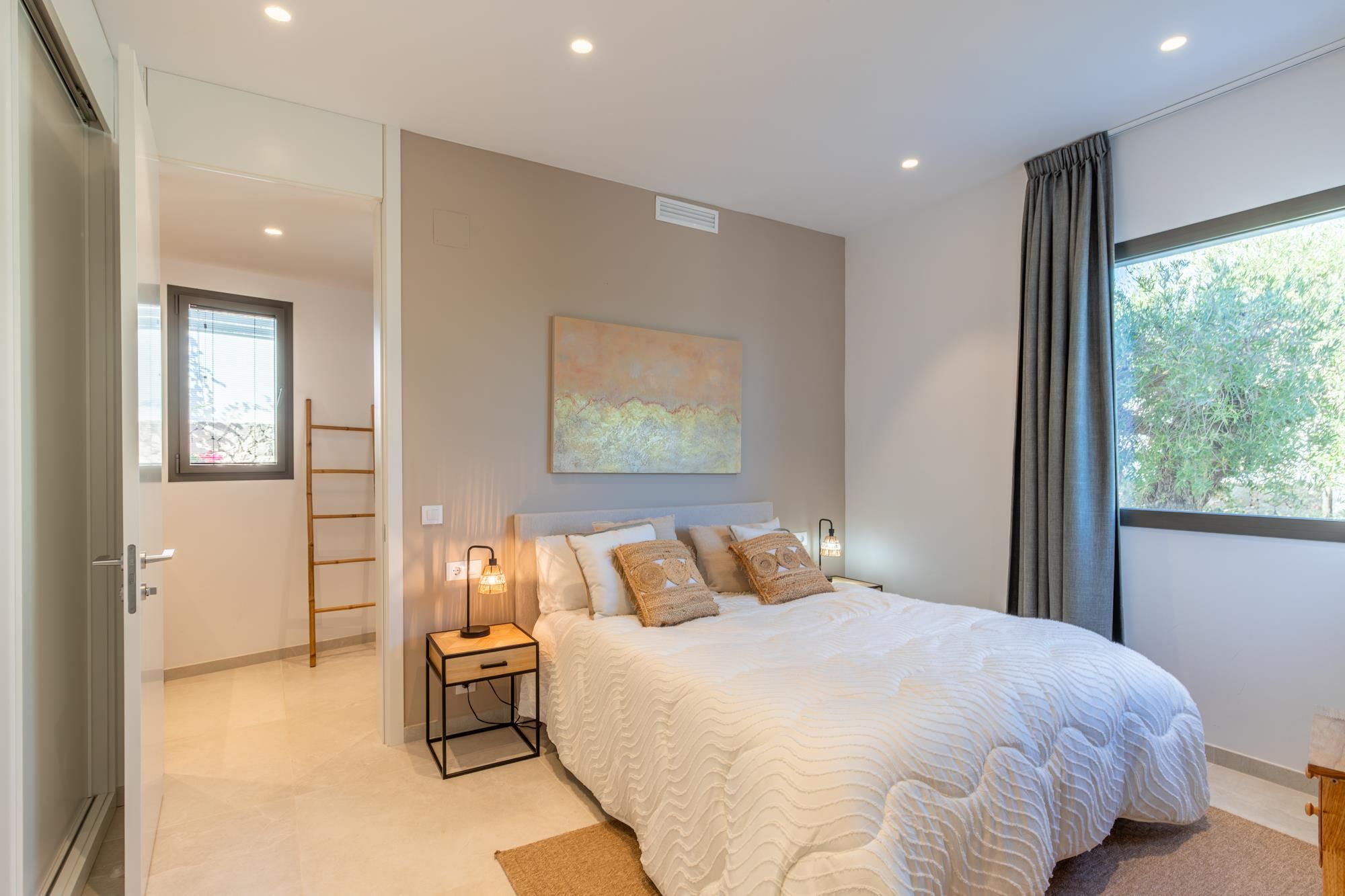 Une chambre à coucher avec un lit, une table de chevet, une lampe et une fenêtre avec des rideaux.