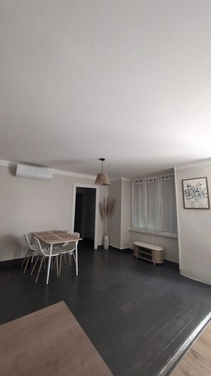 A dining area with a table and chairs, a hanging light fixture, a window with curtains, and a wall-mounted air conditioner. - New Listing (Annonay)