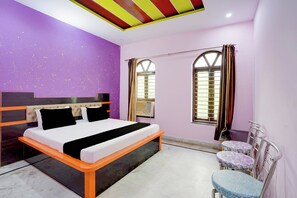 A bedroom with a bed, a window with curtains, and a small table with a chair. - Hotel O Devi Kripa (Mathura)