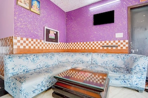 A room with a purple wall, a checkered pattern at the base, a sofa with a floral pattern, and a television mounted on the wall. - Hotel O Devi Kripa (Mathura)