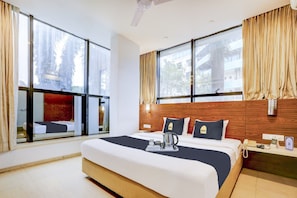 A hotel room with a large bed, two bedside tables, a wooden headboard, and large windows with curtains. - Collection O by OYO Suncity Premiere (Mumbai)