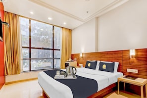 A hotel room with a large window, a bed with two pillows, a bedside table with a lamp, and a tray with a kettle and cups. - Collection O by OYO Suncity Premiere (Mumbai)