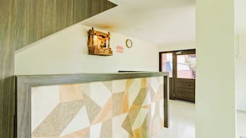A reception area with a geometric patterned wall, a wooden reception desk, a wall-mounted clock, and a door leading to another room.