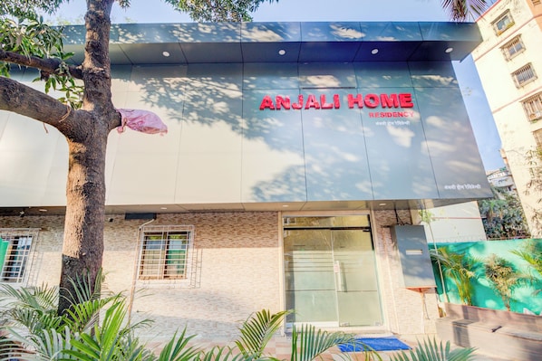 Un edificio con un letrero que dice 'ANJALI HOME RESIDENCY' y un árbol en primer plano.