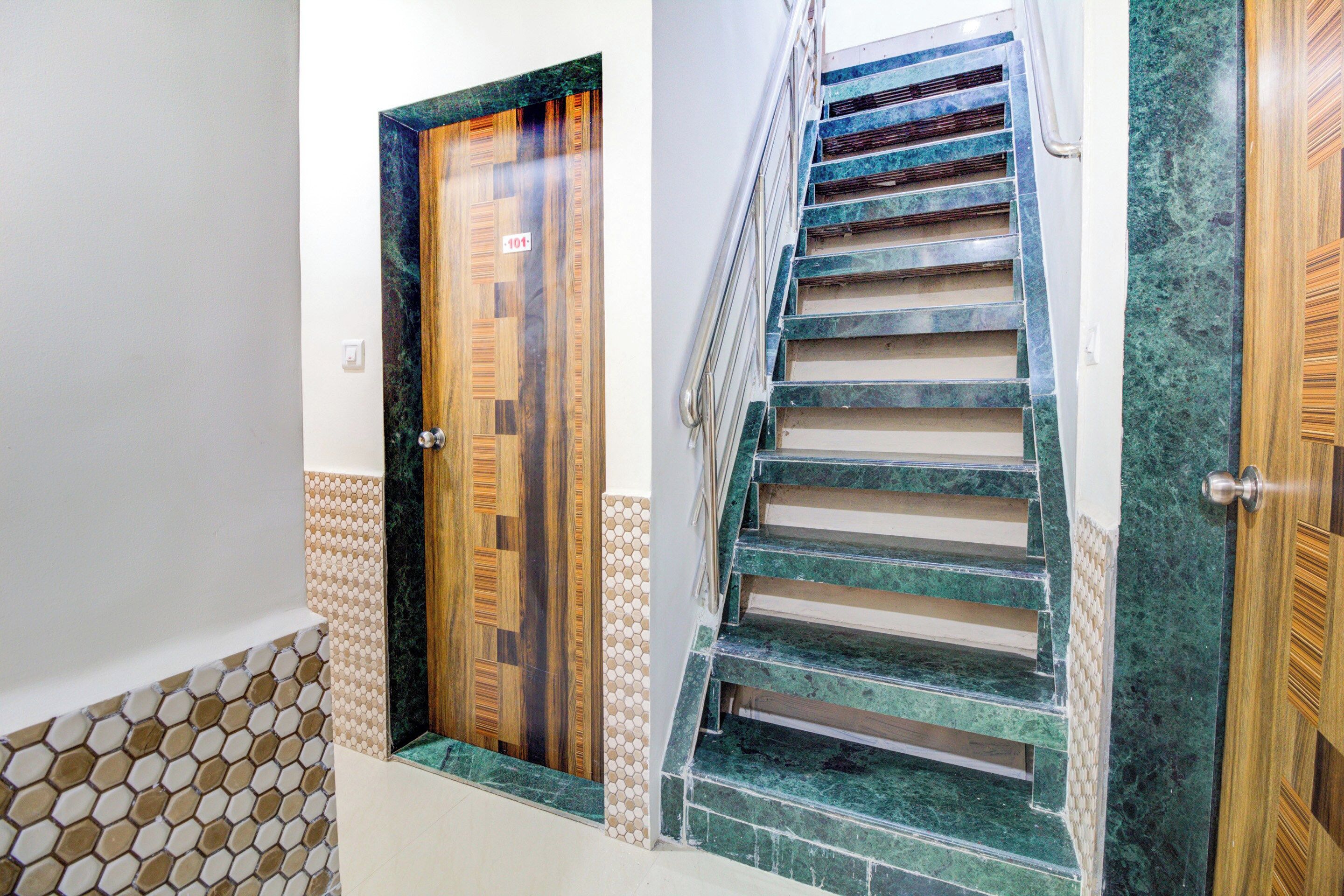 Un pasillo con dos puertas de madera, una con un letrero de número, y una escalera con escalones de mármol verde.