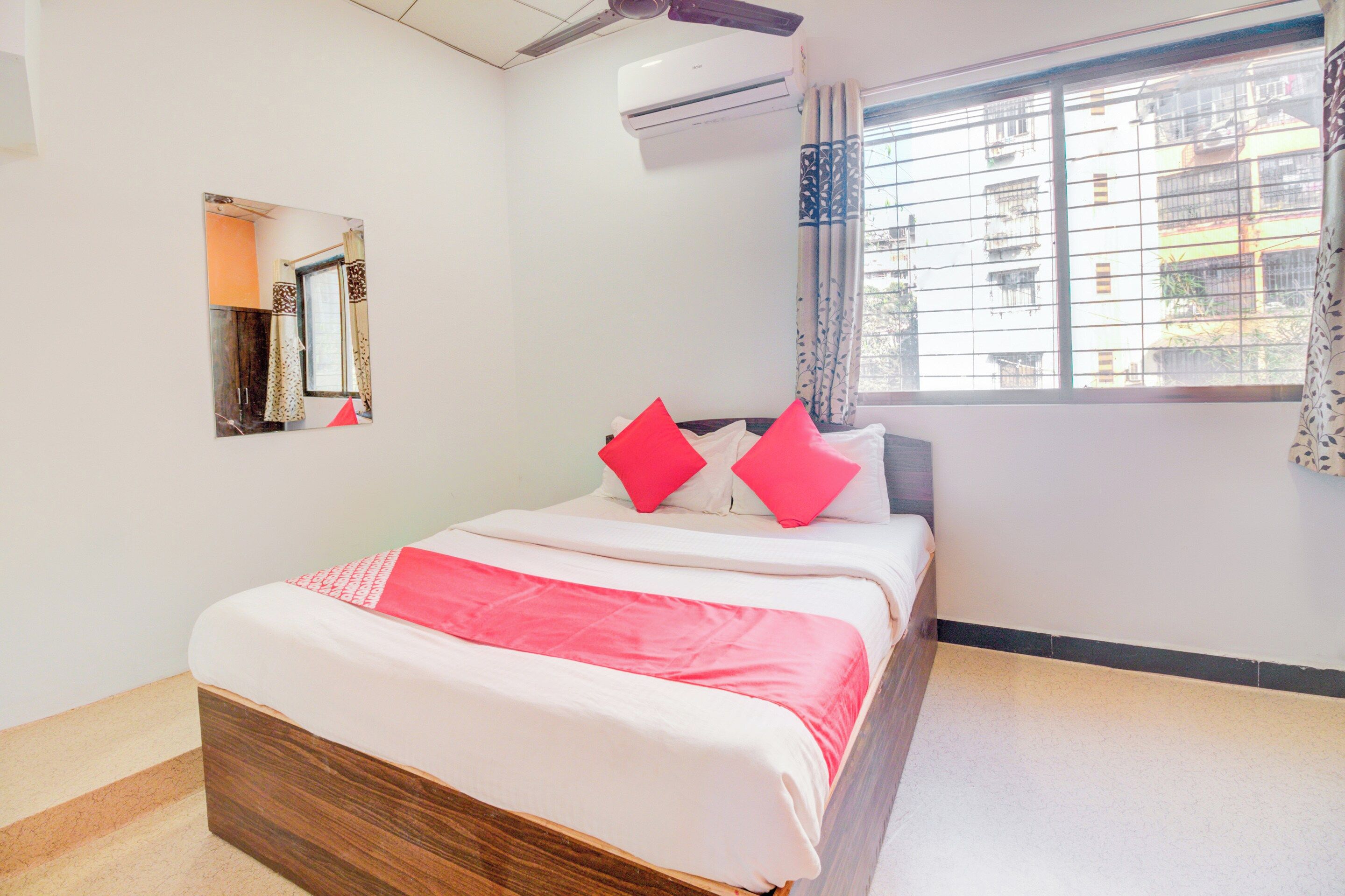 Habitación de hotel con cama, ventana con cortinas, unidad de aire acondicionado y un espejo en la pared.