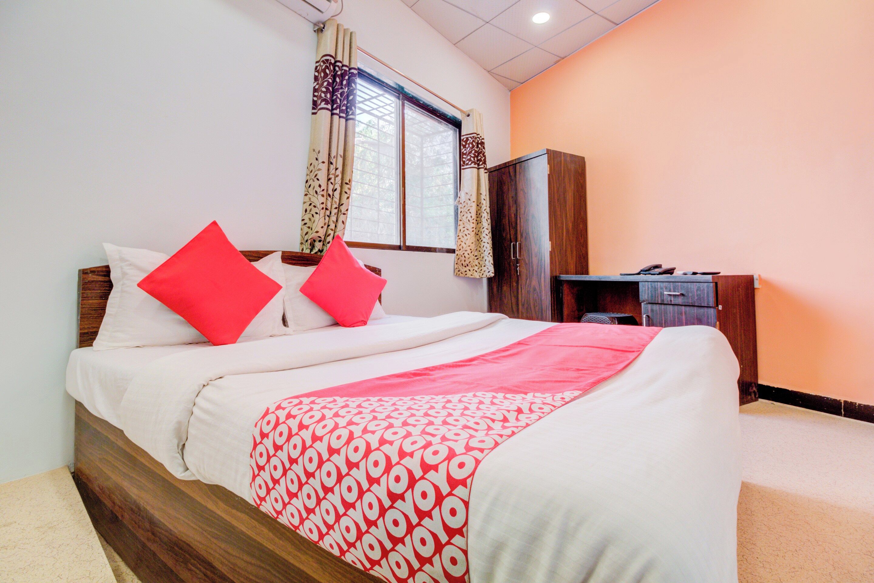 Una cama bien hecha con una colcha estampada, un escritorio con una silla y un armario en una habitación con ventana y cortinas.
