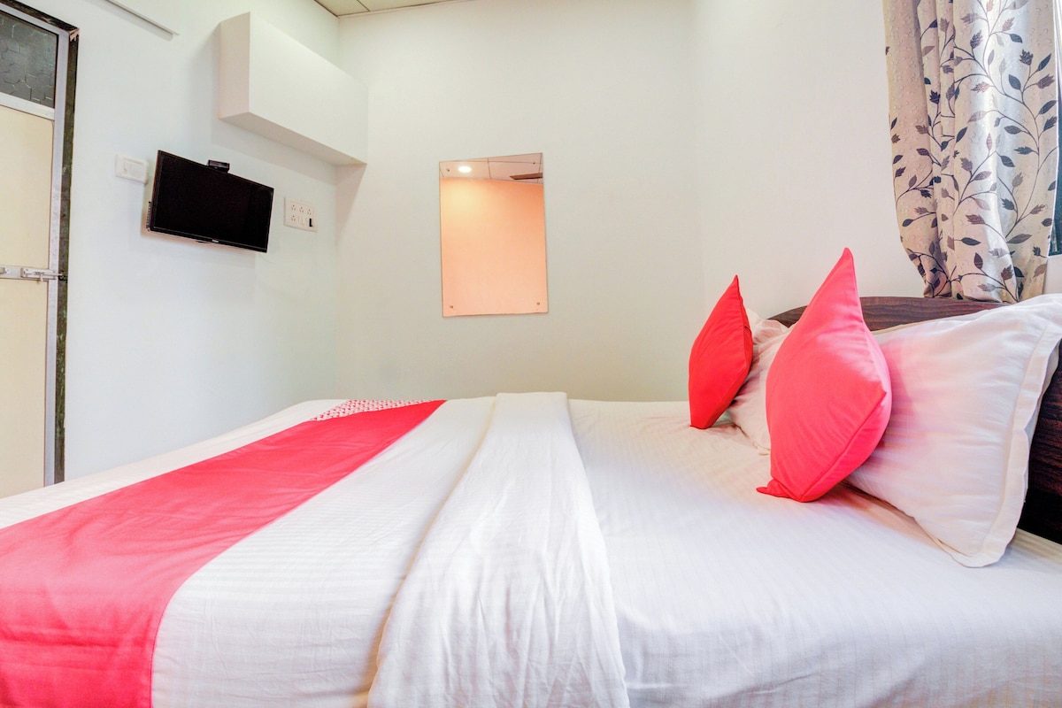 Una camera d'albergo con un letto, una televisione a schermo piatto montata al muro e una finestra con tende.
