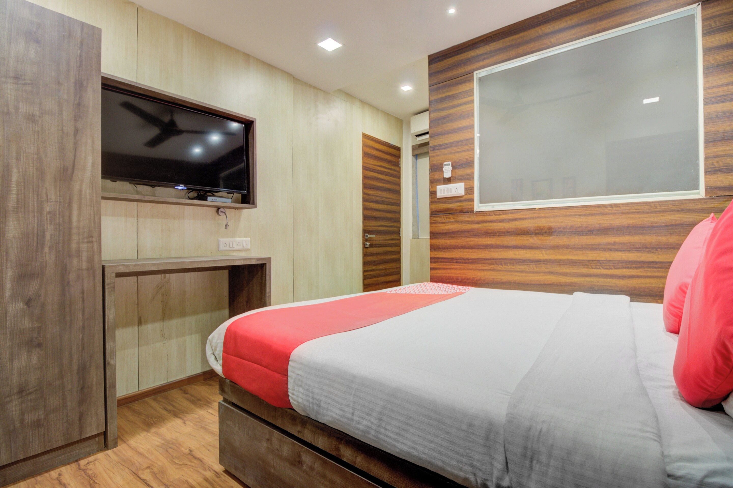 A hotel room with a bed, a television mounted on the wall, and a window.