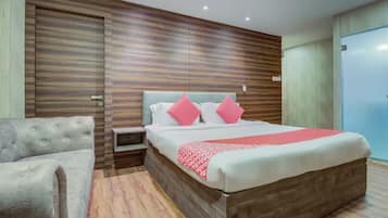Une chambre moderne avec une tête de lit en bois, un lit avec une literie blanche et des touches de rouge, une table de chevet et un fauteuil gris.