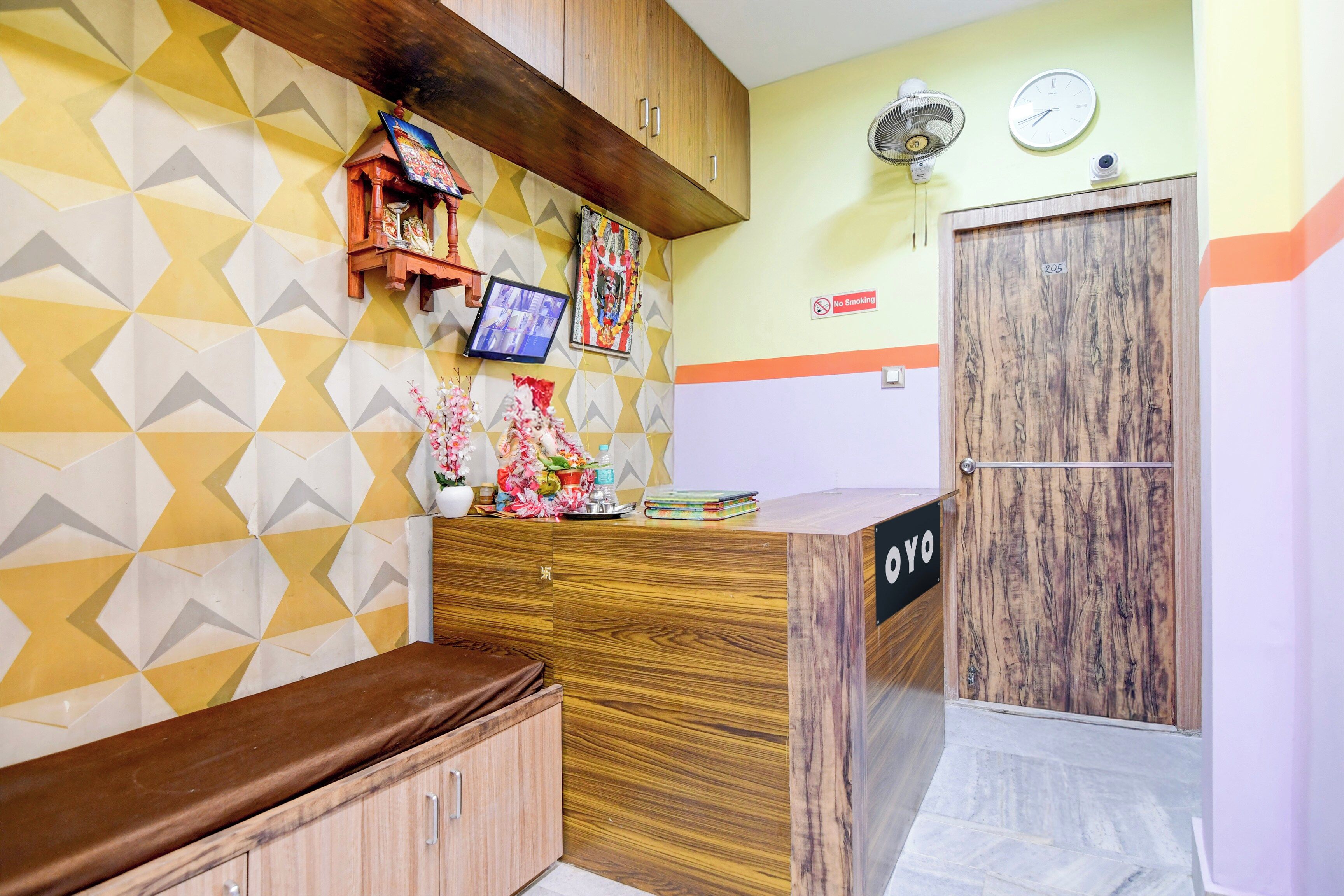 Un espace d’accueil avec un comptoir en bois, un panneau « Il est interdit de fumer », une horloge et une caméra de surveillance fixée au mur.