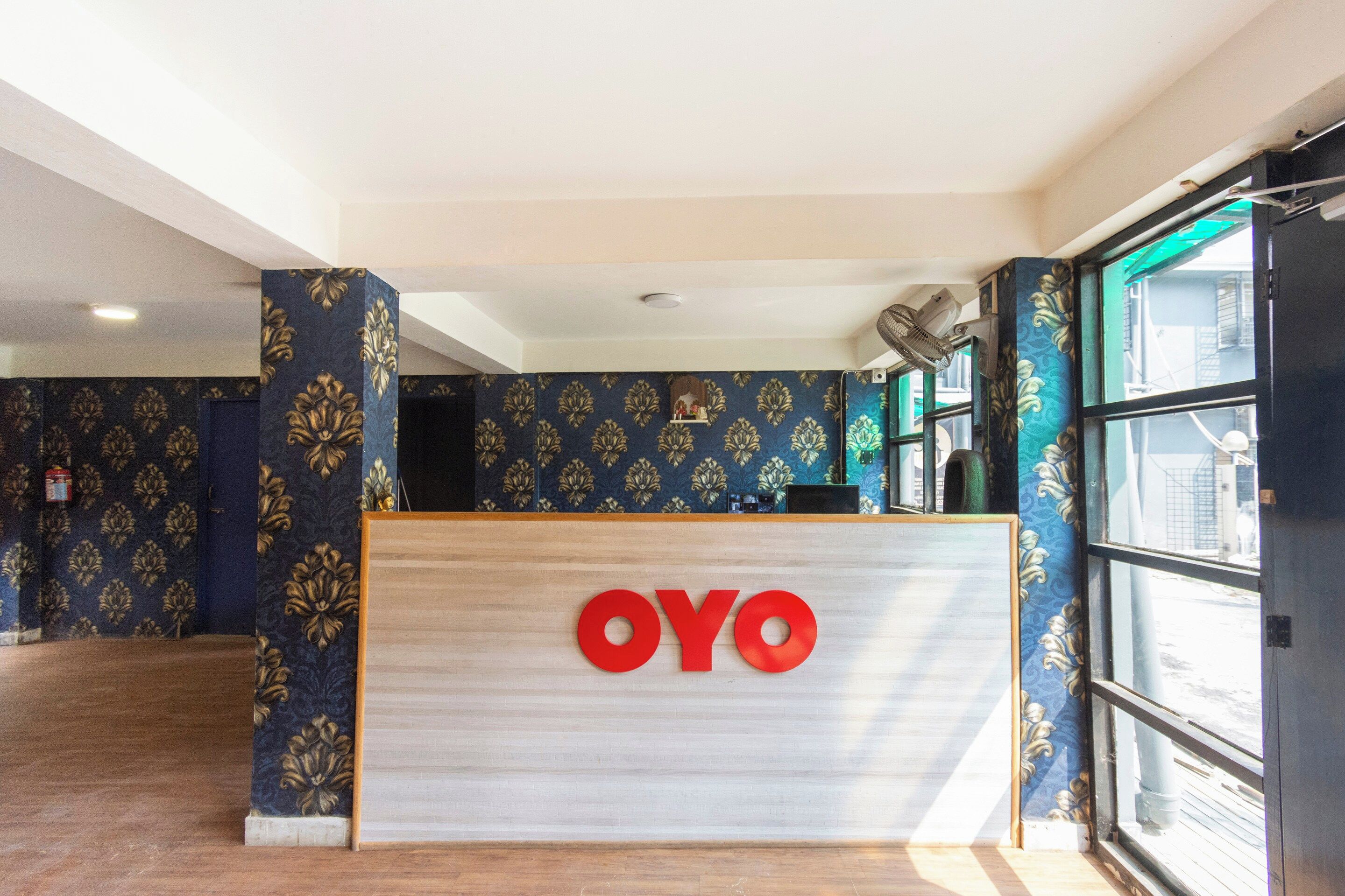 Un comptoir d’accueil arborant le logo « OYO », un mur décoré d’un motif et une grande fenêtre offrant une vue dégagée.