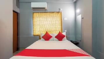 Habitación de hotel con cama, mesita de noche, espejo, aire acondicionado y ventana con cortina estampada.