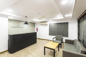 Zona de recepción con mostrador, ventilador de techo, unidad de aire acondicionado, extintor y asientos.