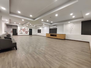 Una habitación amplia con piso de madera, un sofá, un televisor sobre un mueble de madera y una puerta que da a otra área.
