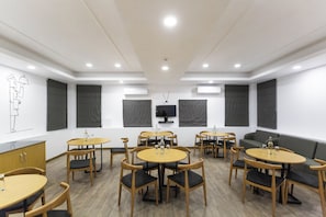 Un salón de conferencias con mesas redondas, sillas, un sofá y un equipo de aire acondicionado.