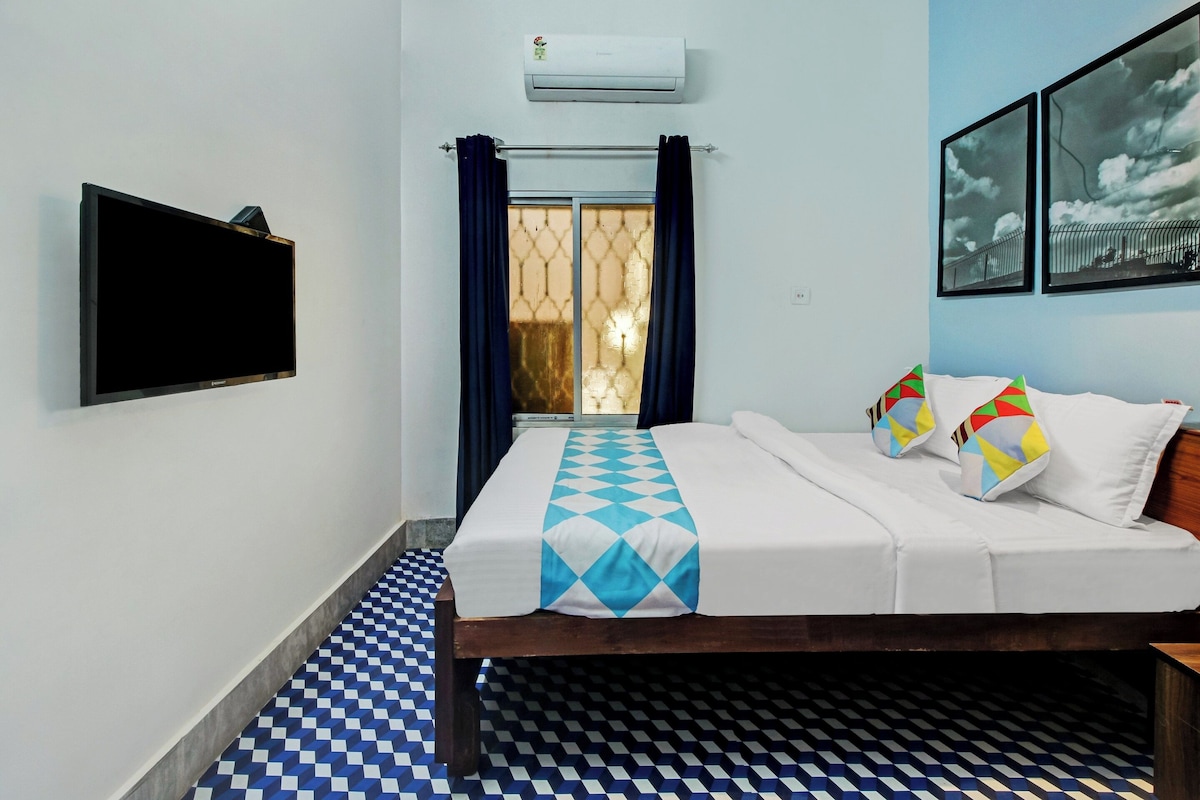 Una habitación de hotel con una cama, un televisor de pantalla plana, un ventanal con cortinas y un suelo estampado.