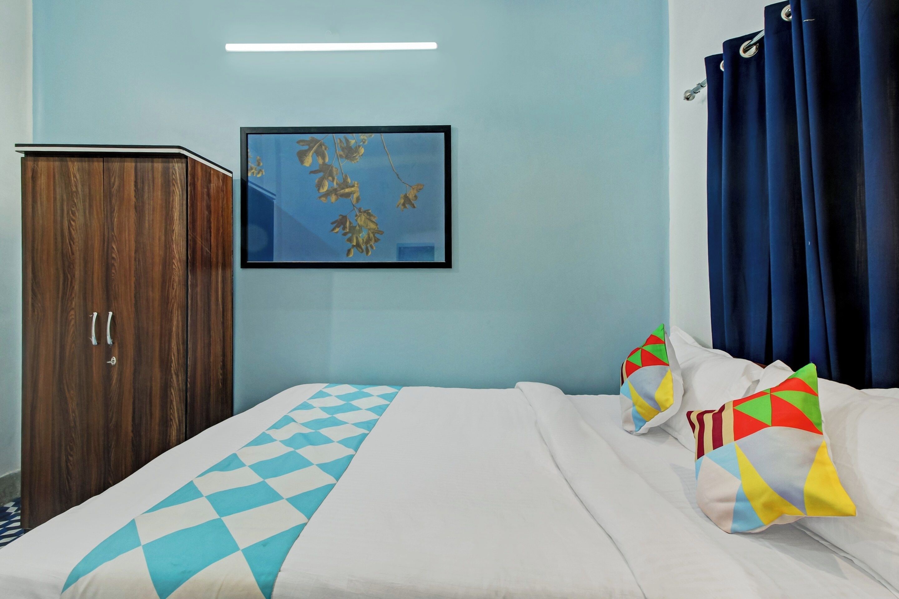 Ein Hotelzimmer mit einem Bett, einem Schrank, einem gerahmten Bild an der Wand und blauen Vorhängen.