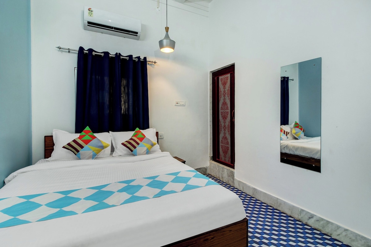 A bedroom with a bed, a mirror, a window with curtains, and an air conditioning unit.