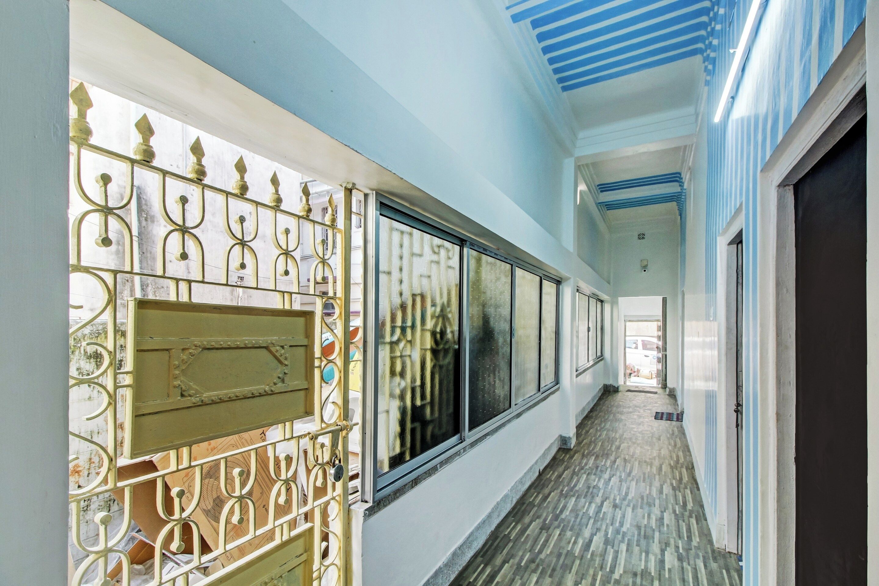 Un pasillo con una reja metálica decorativa, ventanas amplias y piso de baldosas.