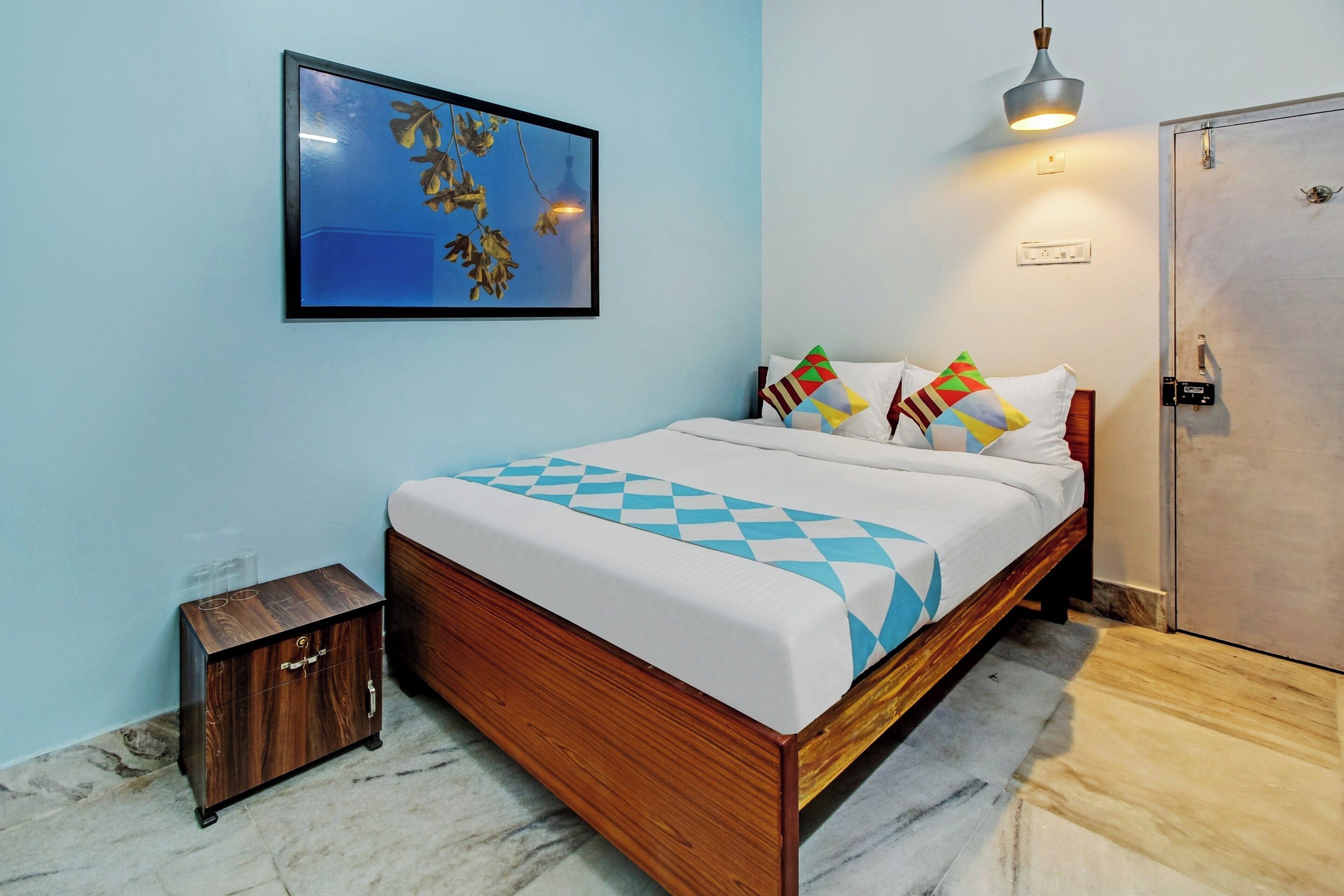 Un dormitorio con cama de madera, una mesita de noche pequeña, un armario, un cuadro en la pared y una lámpara colgante.