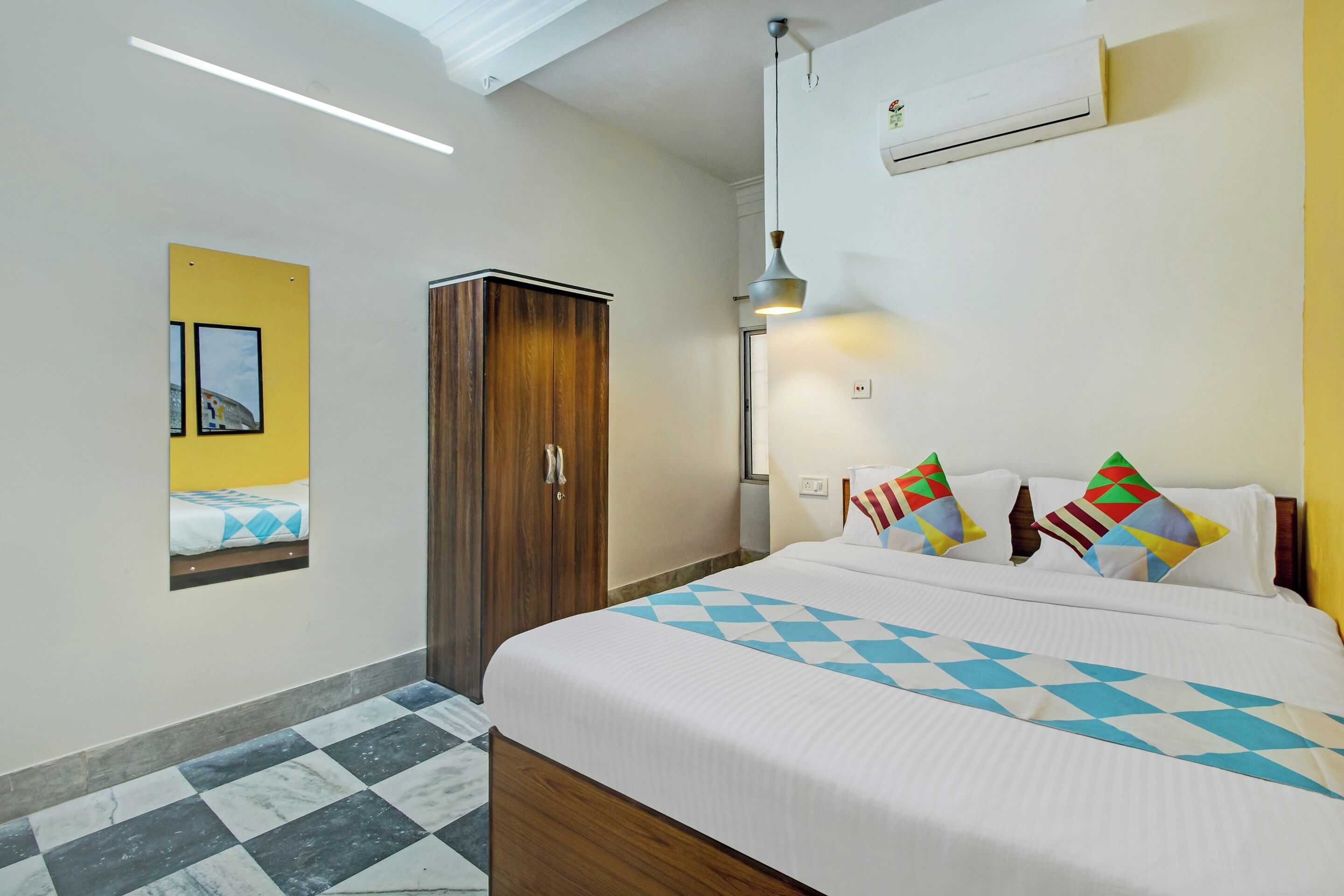 Habitación de hotel con una cama, armario, aire acondicionado instalado en la pared y un marco de fotos.