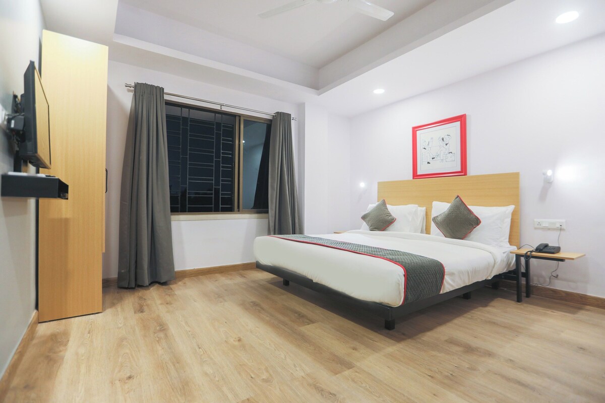 Quarto de hotel com cama, mesa de cabeceira com telefone, janela com cortinas e um quadro na parede.