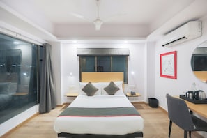 Ett hotellrum med en säng, ett sängbord, ett skrivbord, en stol och ett stort fönster.