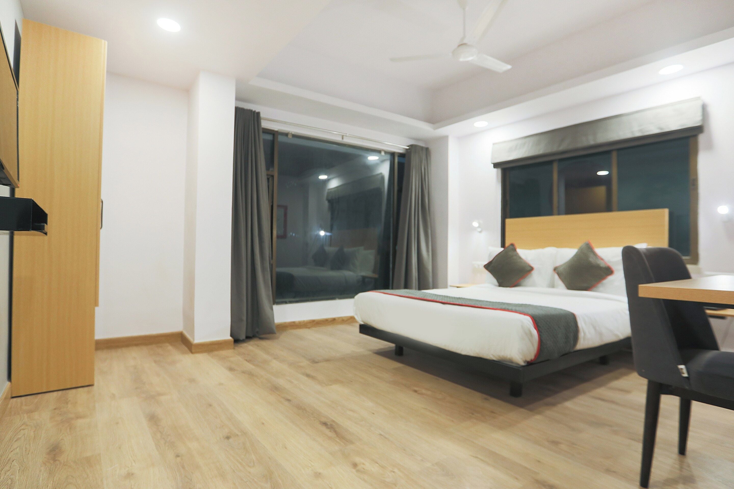 A hotel room with a bed, a desk, a chair, a window with curtains, and a ceiling fan.
