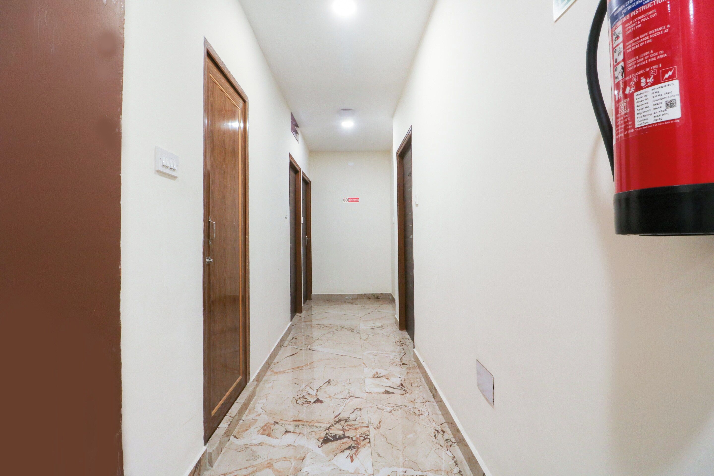 A hallway with marble flooring, wooden doors, and a fire extinguisher mounted on the wall.