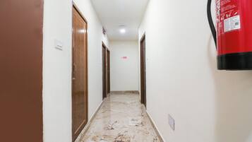 A hallway with marble flooring, wooden doors, and a fire extinguisher mounted on the wall.