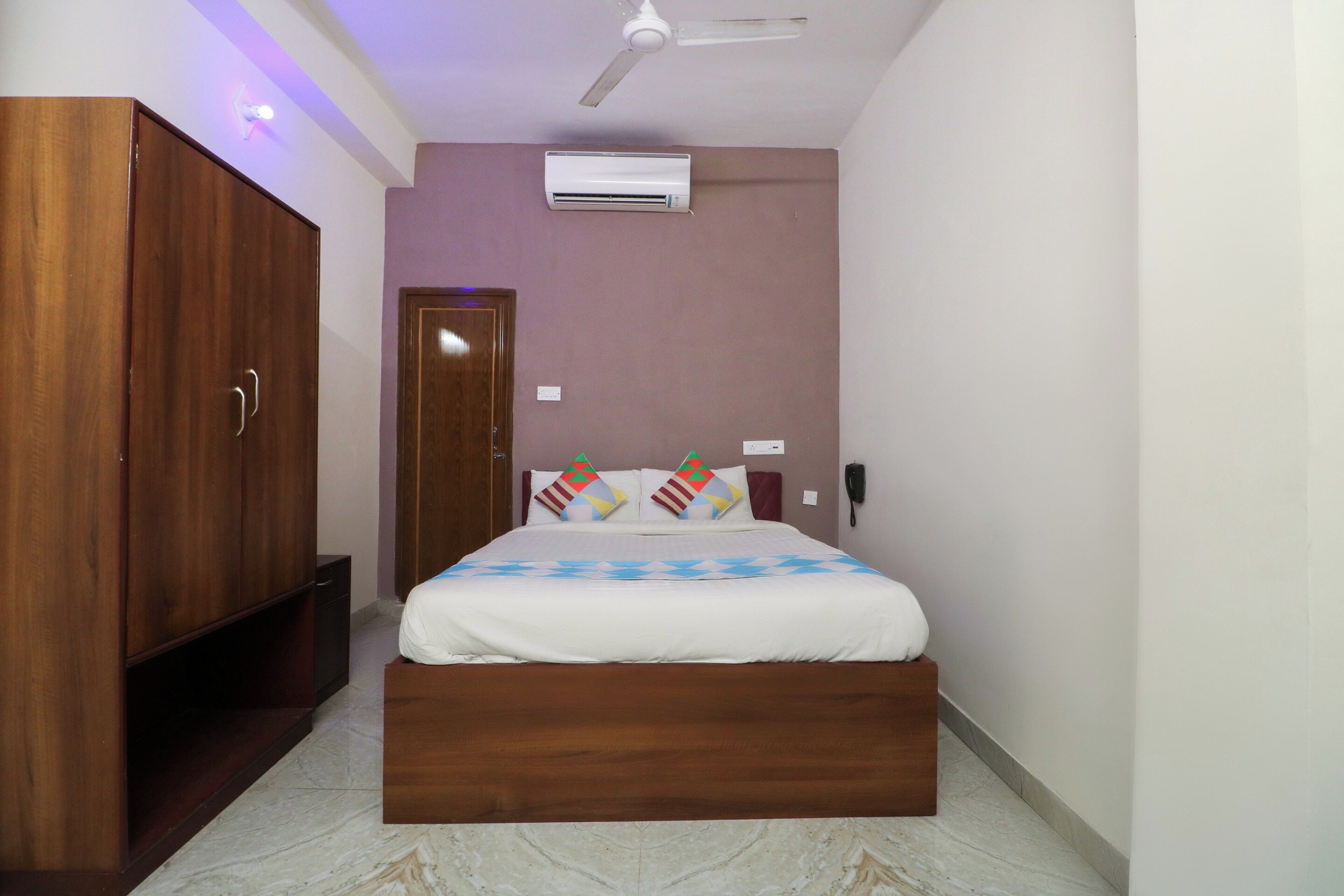 A bedroom with a bed, wooden wardrobe, air conditioning unit, and a ceiling fan.