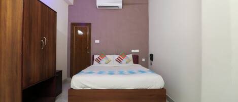 A bedroom with a bed, wooden wardrobe, air conditioning unit, and a ceiling fan.
