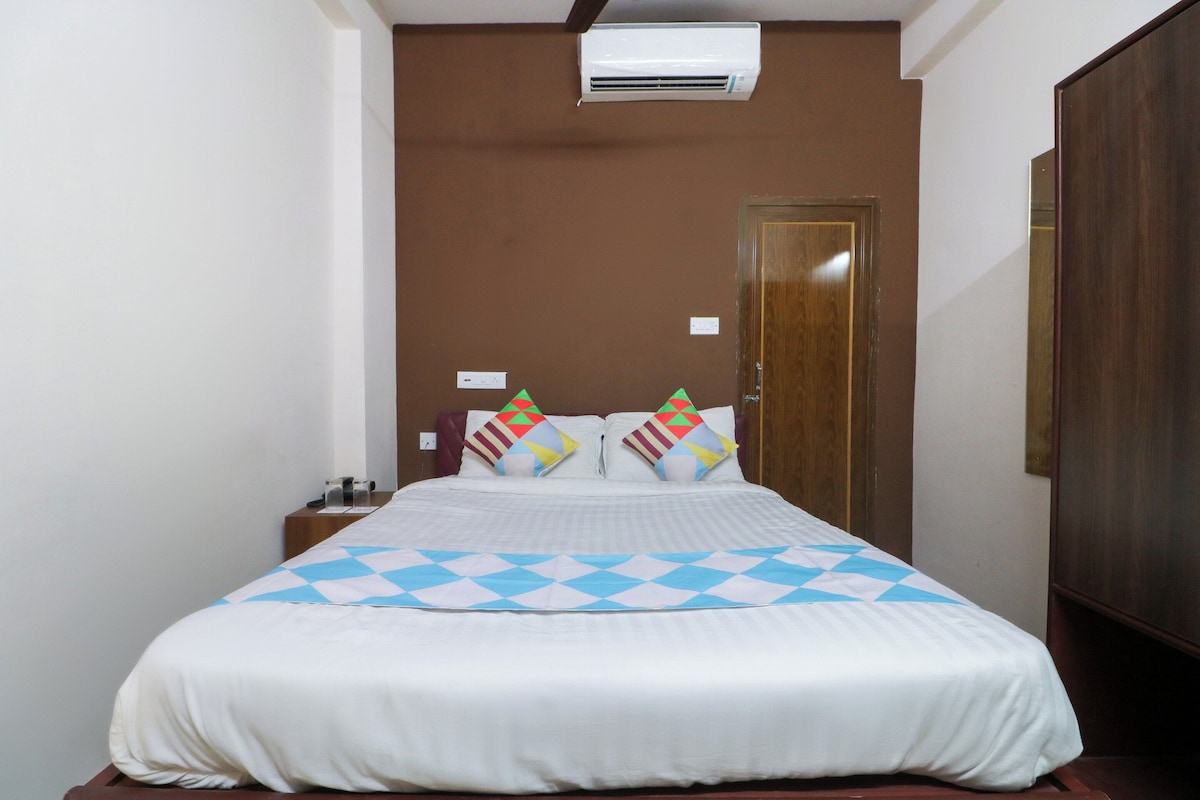 Una habitación de hotel con una cama, una mesita de noche, un armario de madera y un equipo de aire acondicionado en la pared.