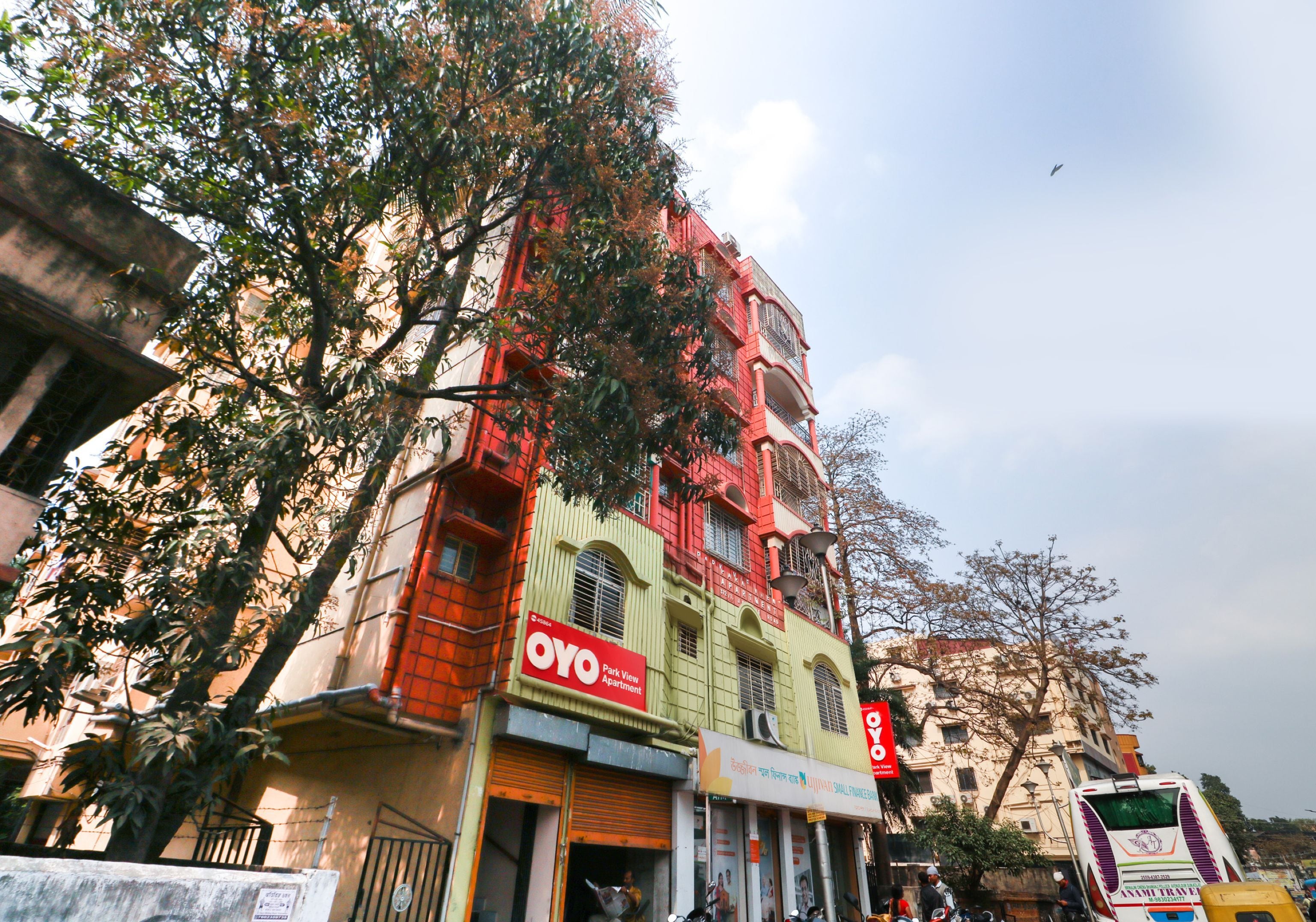 Un edificio de varios pisos con una fachada llamativa de color rojo y verde, un letrero visible que dice 'OYO Park View Apartment' y una pequeña tienda con entrada protegida por un toldo.
