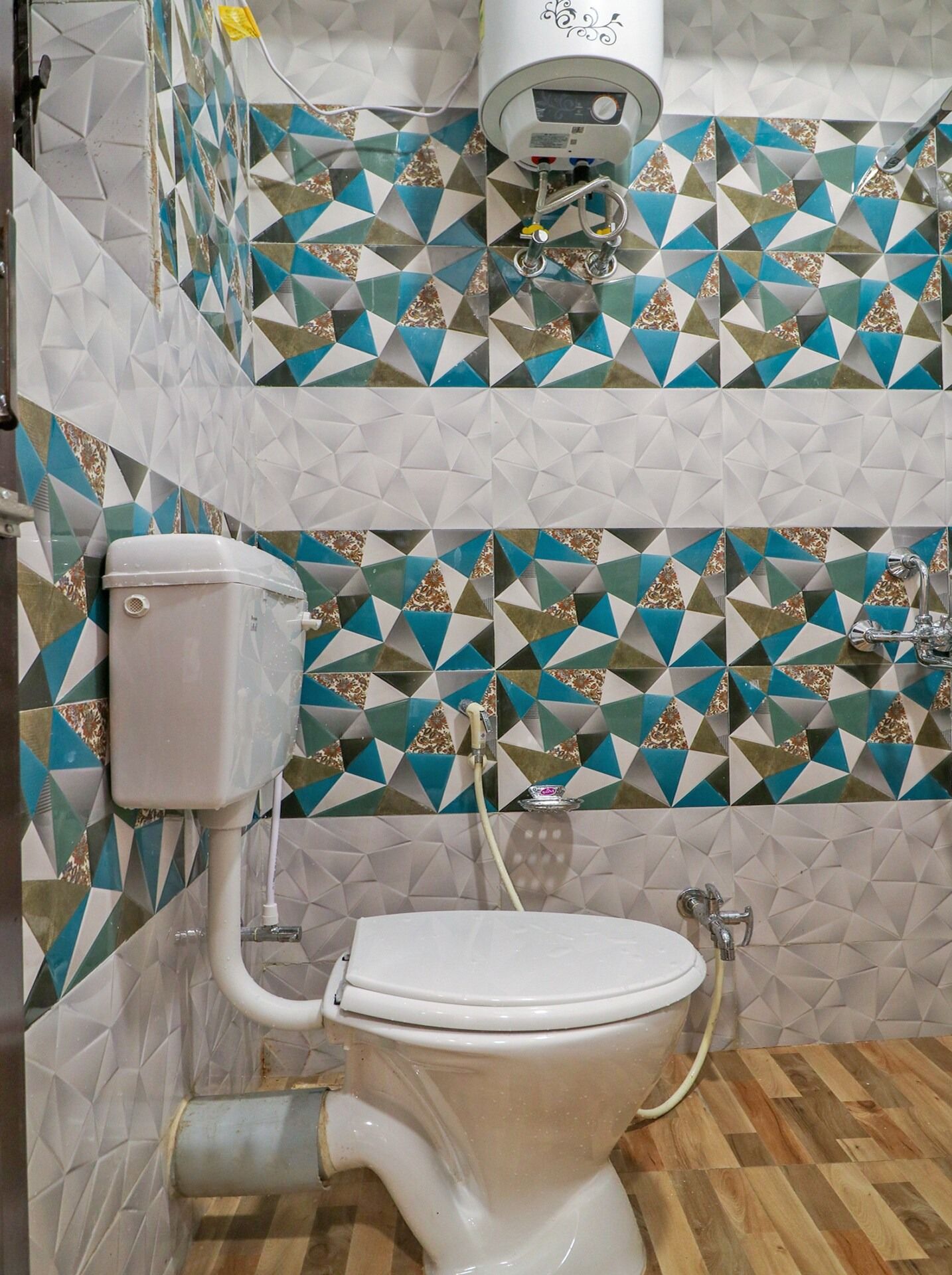 Un baño con inodoro, ducha y pared con baldosas de diseño geométrico.